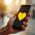 Main tenant un smartphone avec emoji cœur jaune